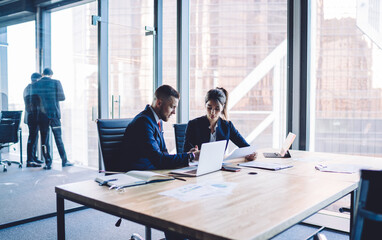 Caucasian male and female business persons sitting at table desktop with modern technology for...