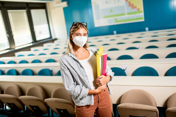 Female student wearing face protective medical mask for virus protection standing at lecture hall