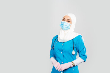  friendly Muslim doctor or nurse wearing hijab and medical face mask and gloves on a gray background.