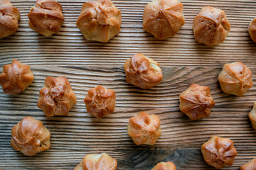 Homemade custard profiteroles laid out on a wooden background.