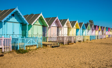 A view along brightly coloured beach huts on West Mersea beach, UK in the summertime