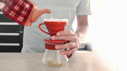 Homemade coffee. Pourover. A man brews at home v 60. He pours hot water into a red ceramic dripper with a filter and coffee drips into a glass server
