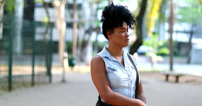 Pensive young black woman standing outside thinking