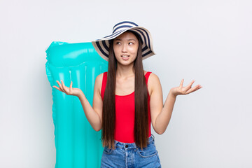 asian young woman shrugging with a dumb, crazy, confused, puzzled expression, feeling annoyed and...