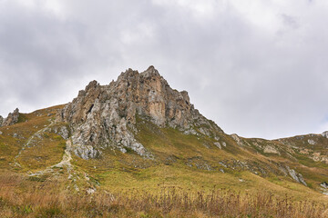 beautiful rocky cliff on a mountain ridge in the distance and an autumn alpine meadow in the foreground