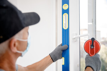 Worker man in medical mask installs plastic upvc windows and doors white with vacuum lifter