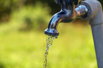 Pouring fresh water  from the metal tap with blurred nature background