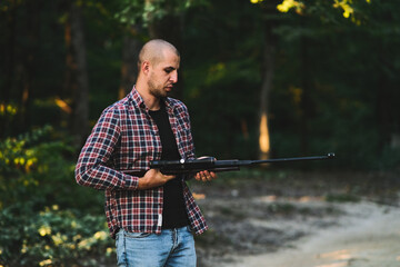 Charismatic guy in a checkered shirt with a weapon. In the autumn forest. Home protection alone