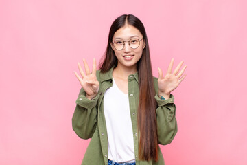 asian young woman smiling and looking friendly, showing number nine or ninth with hand forward,...