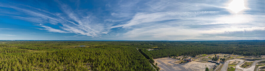 Fototapeta na wymiar Breathtaking Aerial View of Endless Scandinavian green pine tree forest up to horizon line, speedway training track at right side. Sunny summer day, Typical Northern Scandinavia landscape