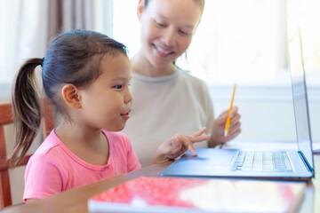 Parent and child doing school work with notebook and computer at home. Homeschooling online.