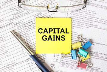 Yellow sticker with text Capital Gains. Next to it is a blue pen with colored stationery clips and...