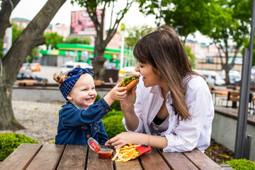 Pretty young mother and daughter eating a big burger at a cafe