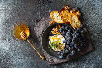 Roast camembert and honey with black grapes and baked slice of bread on dark background