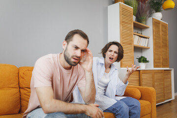 Fototapeta na wymiar Displeased dissatisfied angry irritated young couple two friends man woman 20s in casual clothes sitting on couch screaming swearing spreading hands looking aside spending time in living room at home.