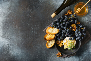 Roast camembert and honey with black grapes and baked slice of bread on dark background