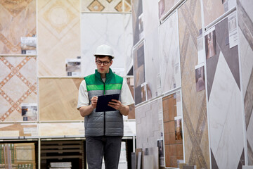 caucasian man is checking supplies on document with an engrossed expression in warehouse, in uniform