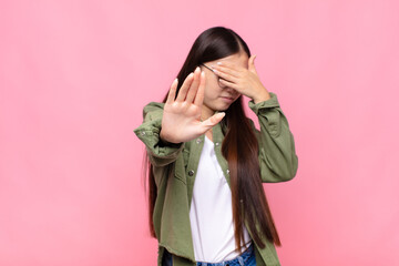 asian young woman covering face with hand and putting other hand up front to stop camera, refusing...