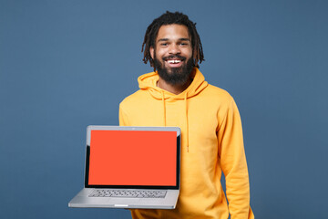 Cheerful young african american man guy in yellow streetwear hoodie posing isolated on blue...