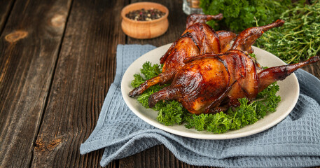 Baked quail with herbs on a wooden table. Side view. Banner. Copy space.