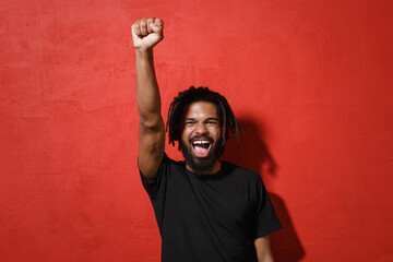 Happy excited young african american man guy with dreadlocks 20s in black casual t-shirt posing...