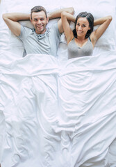 Bedtime. The family are sleeping. Beautiful young couple in love are lying on the big white bed and resting. Husband and wife together in bed. Top view photo
