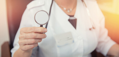Doctor woman holding aStethoscope or phonendoscope on background of white medical gown, preparing to receive patient