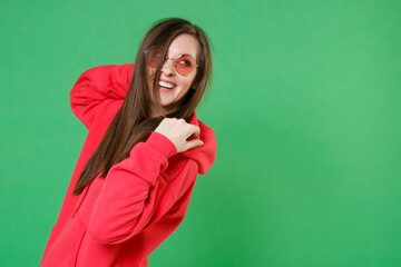 Side view of smiling cheerful laughing beautiful young brunette woman 20s in bright red casual streetwear hoodie eyeglasses posing looking aside isolated on green color background studio portrait.