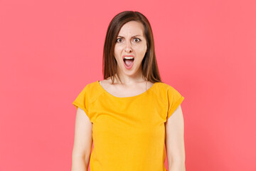 Obraz premium Shocked worried nervous young brunette woman 20s wearing yellow casual t-shirt posing standing looking camera keeping mouth open swearing isolated on pink color wall background studio portrait.