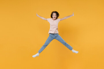 Fototapeta na wymiar Full length portrait of excited happy young woman 20s wearing pastel pink casual t-shirt posing jumping spreading legs and hands looking camera isolated on bright yellow color wall background studio.
