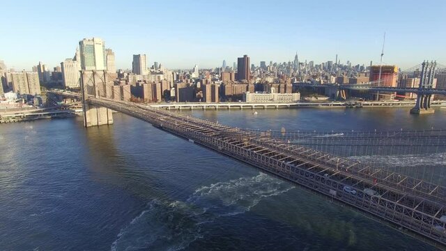 Acercamiento a&eacute;reo al Puente de Brooklyn, con muchos autos circulando, con el skyline de Manhattan como fondo al amanecer.
