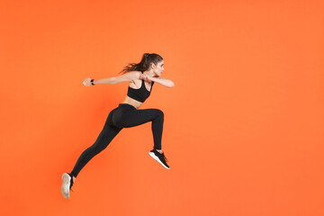 Fototapeta na wymiar Full length side view of portrait of young fitness sporty woman 20s wearing black sportswear posing training working out jumping like running looking aside isolated on orange color background studio.