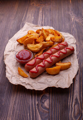 Delicious sausages with fried potatoes and ketchup on a wooden table