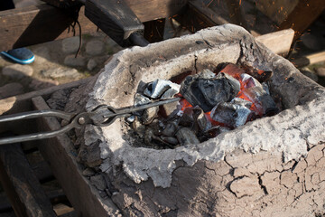 blacksmith sets up the brazier with embers with large coal tongs. Embers glow in a iron forge. Fire, heat, coal and ash