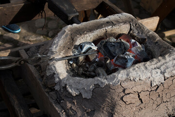 Obraz premium blacksmith sets up the brazier with embers with large coal tongs. Embers glow in a iron forge. Fire, heat, coal and ash