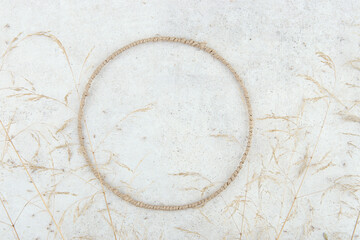 Round jute frame with dried grasses on stone tile background. Composition of dried herb and  circle frame indoor.