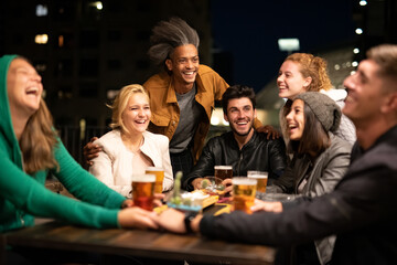 group of friends of different ethnicities meeting to toast with pints of beer, focus on afro boy face, friends are smiling and laughing together, millennial people have a party - obrazy, fototapety, plakaty