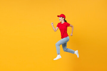 Fototapeta na wymiar Full length body fun delivery employee woman in red cap blank t-shirt uniform work courier in service during quarantine coronavirus covid-19 virus jumping isolated on yellow background studio portrait