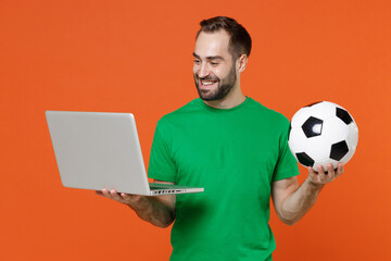 Smiling young man football fan in green t-shirt cheer up support favorite team with soccer ball...