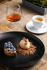 dessert concept, ice cream and cupcake with berries on a black plate, coffee with brandy on the table