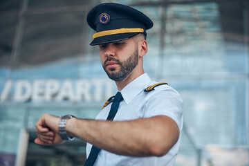 Handsome male pilot looking at wristwatch on the street