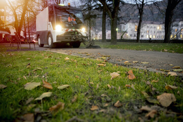 New generation of small electric street sweeper removing fallen leaves in body at autumn city park....