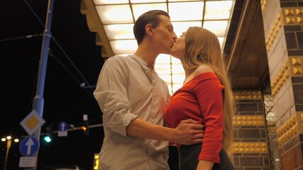 Cute young couple after night date walk saying goodbye kiss and hug and go to the sides on night city street sidewalk under building lights