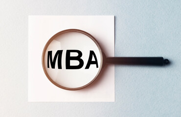 Business educatuion concept. paper sticker with text MBA acronym through magnifying glass on blue...