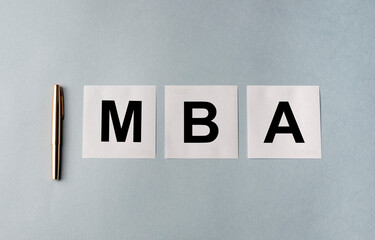 Business educatuion concept. white papers with text MBA acronym on blue grey office table with...