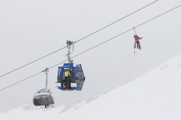 Fototapeta na wymiar Heroes rescue teams on a chairlift at ski resort on the Dolomites. Emergency rescue passengers with the use of ropes and safety ladders in bad weather winter conditions. Foggy day. 