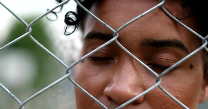Sad black woman seen through metallic fence cage