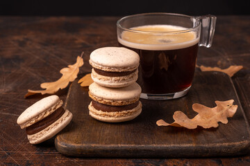 Glass cup of coffee and chocolate macarons on wooden background. Cozy autumn composition