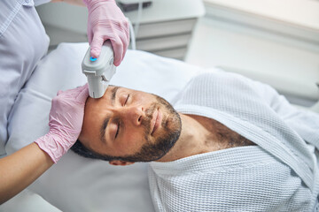 Obraz na płótnie Canvas Female esthetician treating male skin with laser device