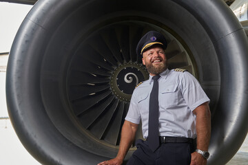 Happy optimistic pilot posing on the plane turbine